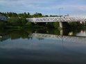 Klidná hladina Orlice mezí říčním prahem a silničním mostem ve Svinarech.